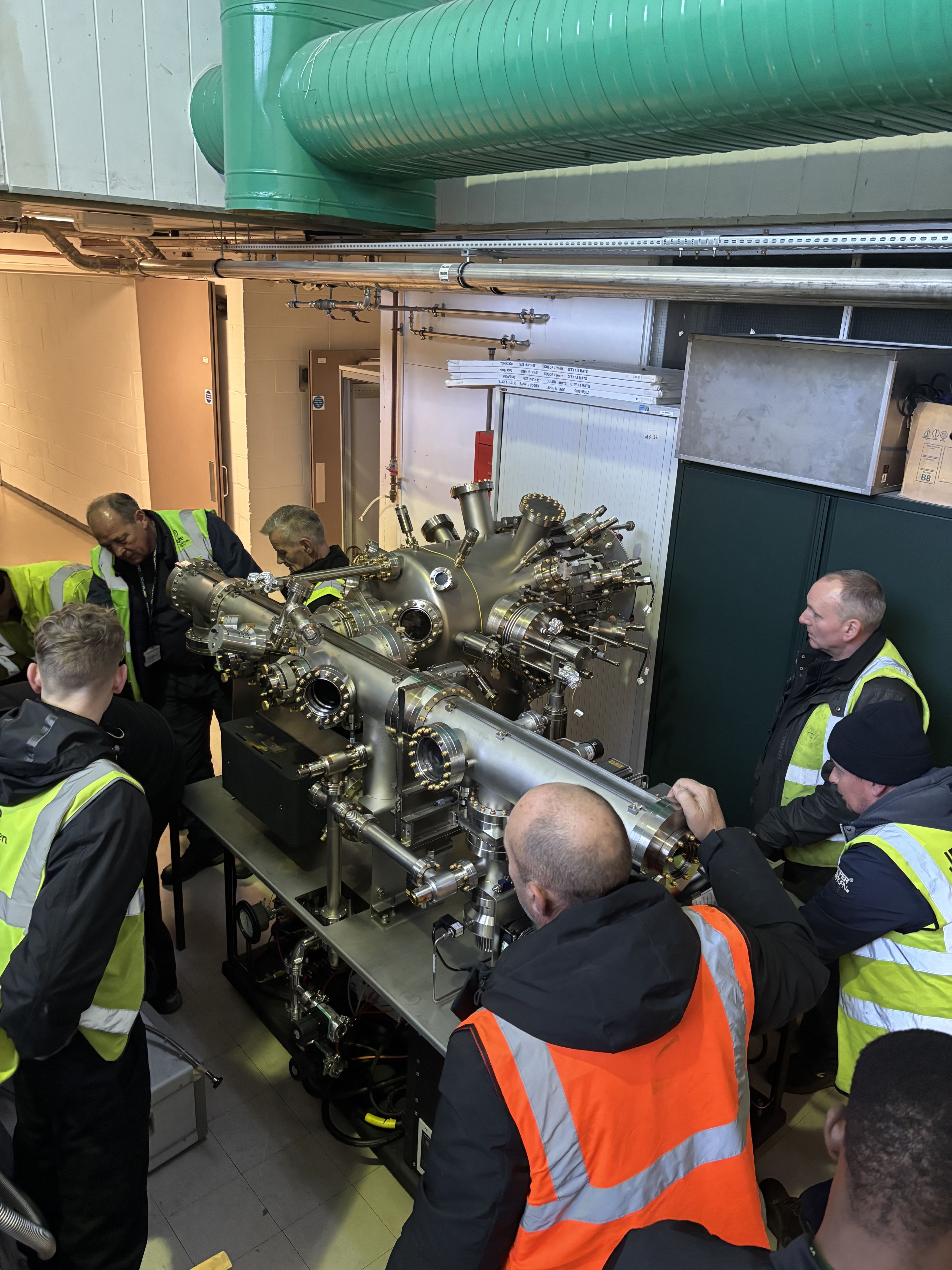 Large piece of equipment moving into the cleanroom, pulled and pushed by men wearing high-visibilty vests