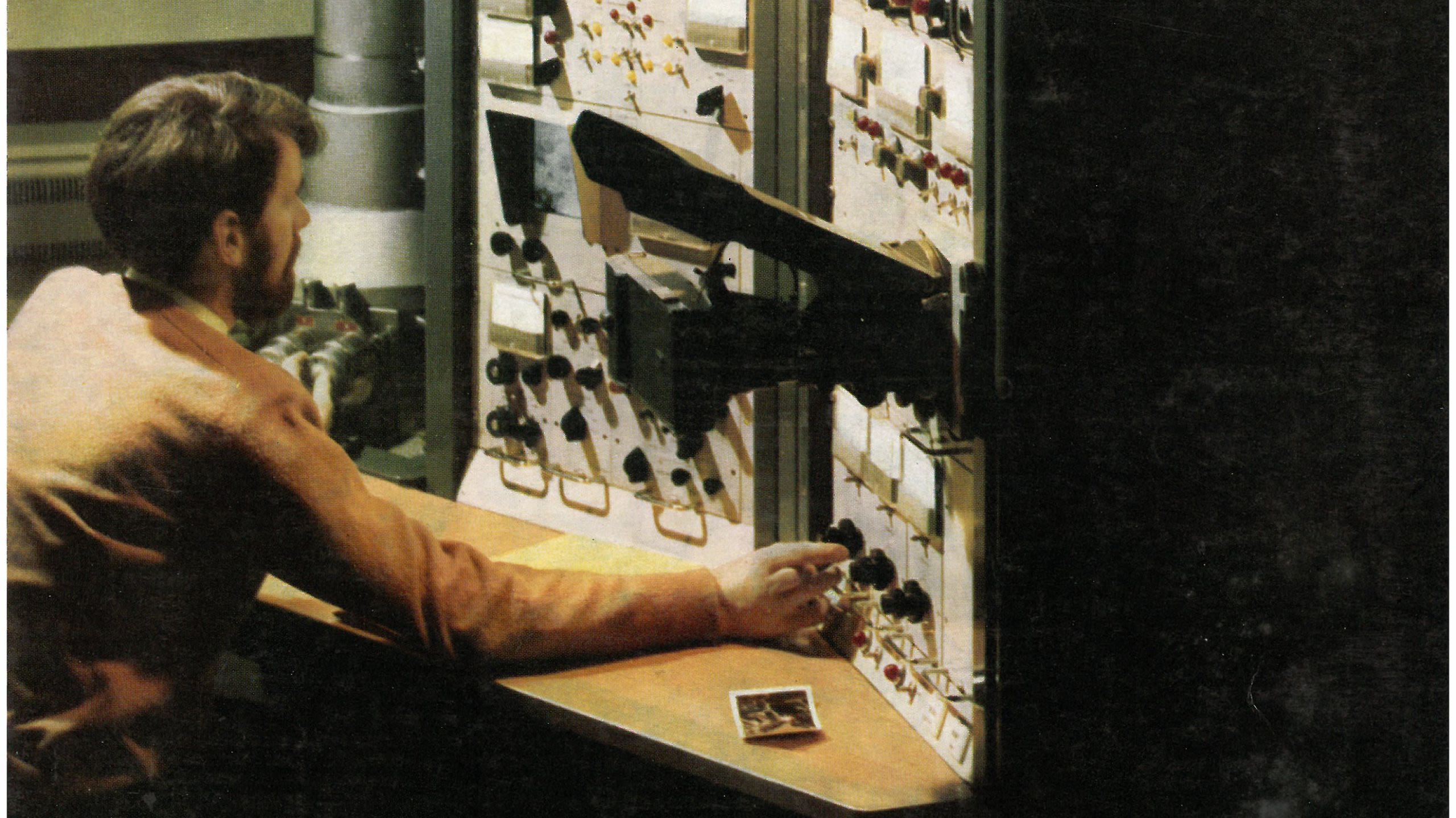 Man sat in front of a vintage electron microscope and turning buttons