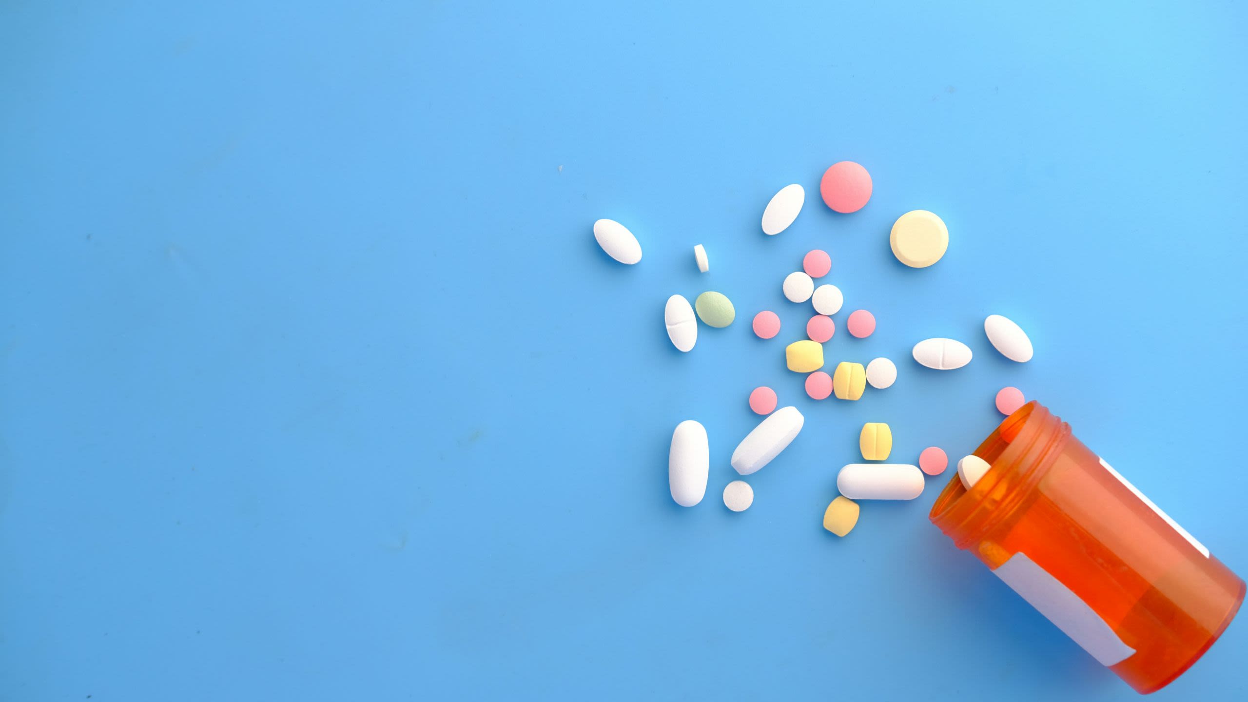 Pills spilling out of a plastic tub on a bright blue background